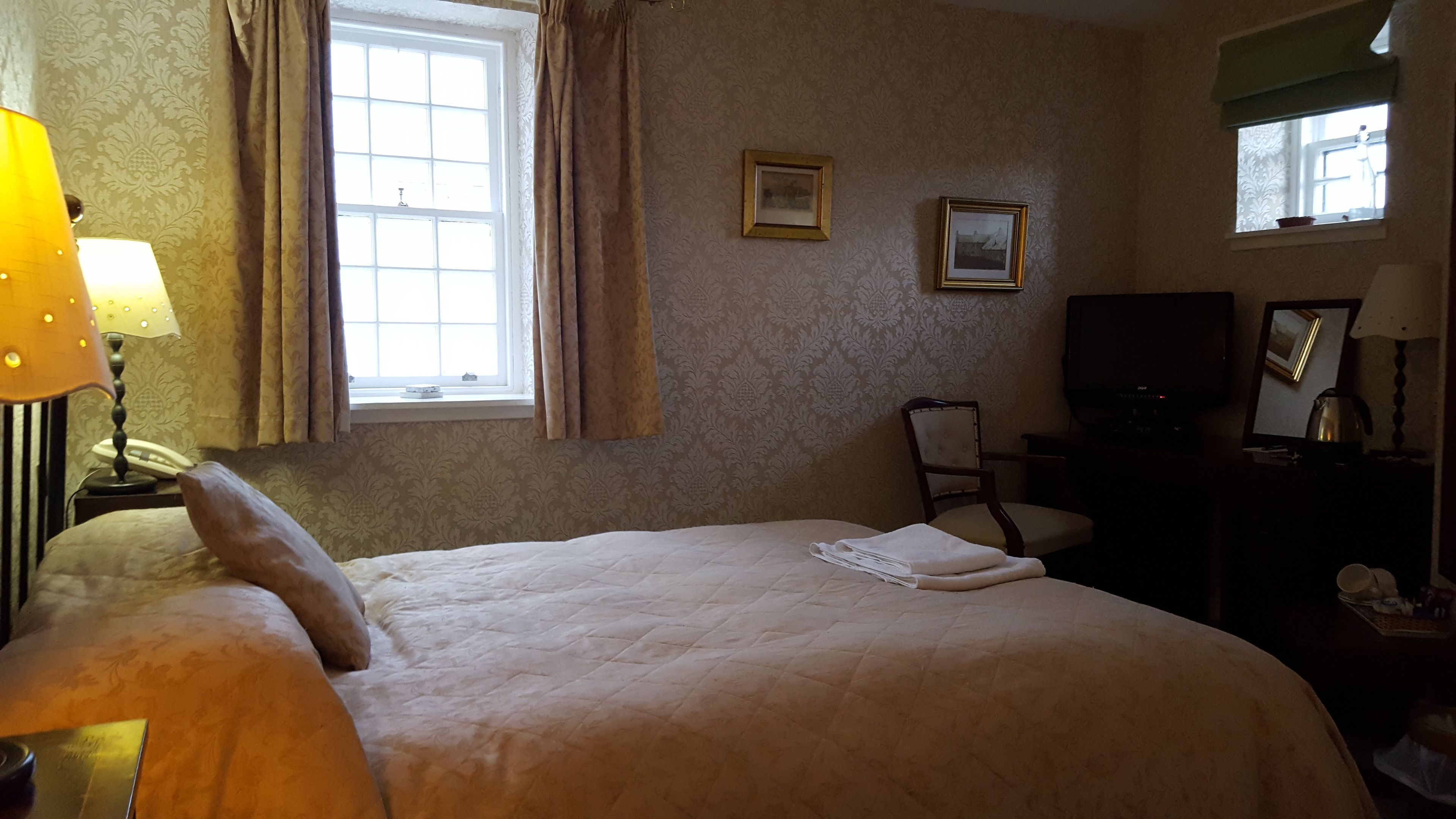 A hotel room with a bed, a chair, a desk with a lamp, a television, and a window with curtains.