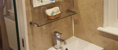 Et badeværelse med en hvid vask, et spejl og en hylde med toiletartikler.