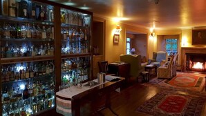 Zona de bar con estantes de botellas de licor, barra y área de estar con sillones y chimenea.