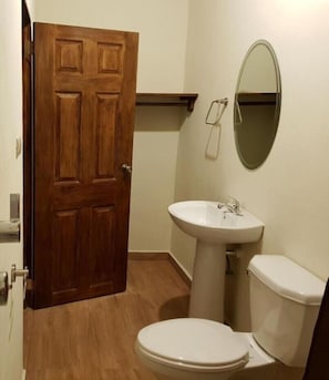 A bathroom with a wooden door, a white sink, a toilet, and a mirror on the wall. - Hostal Deyluwin (Juayua)