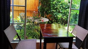 Un comedor con mesa y sillas, una pared de madera y vistas a un jardín exuberante a través de grandes ventanales.