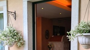 A hotel entrance with a tiled floor, a doormat with heart designs, and a room visible through the doorway featuring a sofa, a table, and hanging plants. - Bed & Breakfast Isonzo (Turriaco)