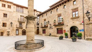 A historic stone building with a courtyard, featuring a central column, potted plants, and a sign indicating a hotel and restaurant. - Hotel Villa de Cretas (Cretas)