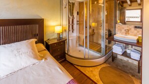 A hotel room with a bed, a glass-enclosed shower, a wooden headboard, a nightstand, and a bathroom with a sink and towel rack. - Hotel Villa de Cretas (Cretas)