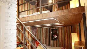 Habitación con varios niveles, una litera, una escalera de madera y una mesita pequeña.