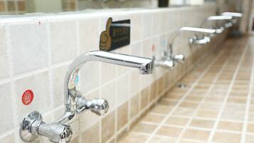 A row of public bathroom sinks with chrome faucets and a sign above them.