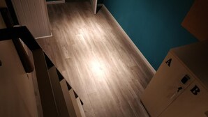 Una habitación con piso de madera, paredes color verde azulado y una puerta que da a otra habitación.