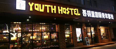 Une auberge de jeunesse avec une enseigne lumineuse, de grandes fenêtres et une façade en briques.