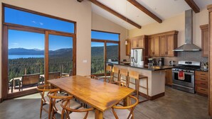 A spacious kitchen with wooden cabinets, a large island, and a view of mountains through large windows. - Beautiful View by Hauserman Rentals (Tahoe City)