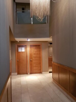 A hallway with two wooden doors, a ceiling light, and a hanging chandelier.