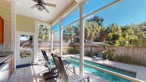 Une terrasse couverte avec une piscine, du mobilier d’extérieur et une vue sur le jardin arrière.