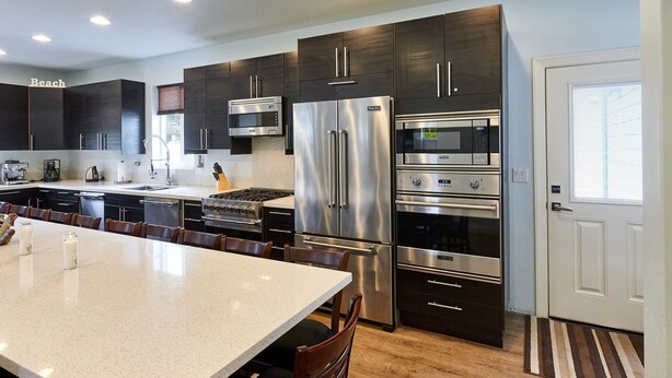 Una cocina moderna con armarios oscuros, electrodomésticos de acero inoxidable, una isla grande y un comedor con sillas.