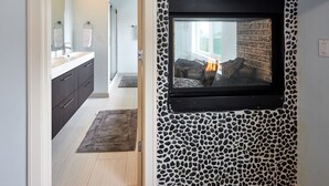 Un baño moderno con pared de diseño de piedra, televisor montado y chimenea a la vista.