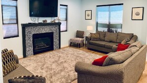 Una sala de estar con chimenea, un conjunto de sofás, televisión y ventilador de techo.