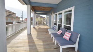 A covered porch with wooden flooring, white railings, and a row of white benches with cushions. - Luxury in Crystal Beach~ 4/3 ~ Beautiful Beach Views~Direct beach access (Crystal Beach)