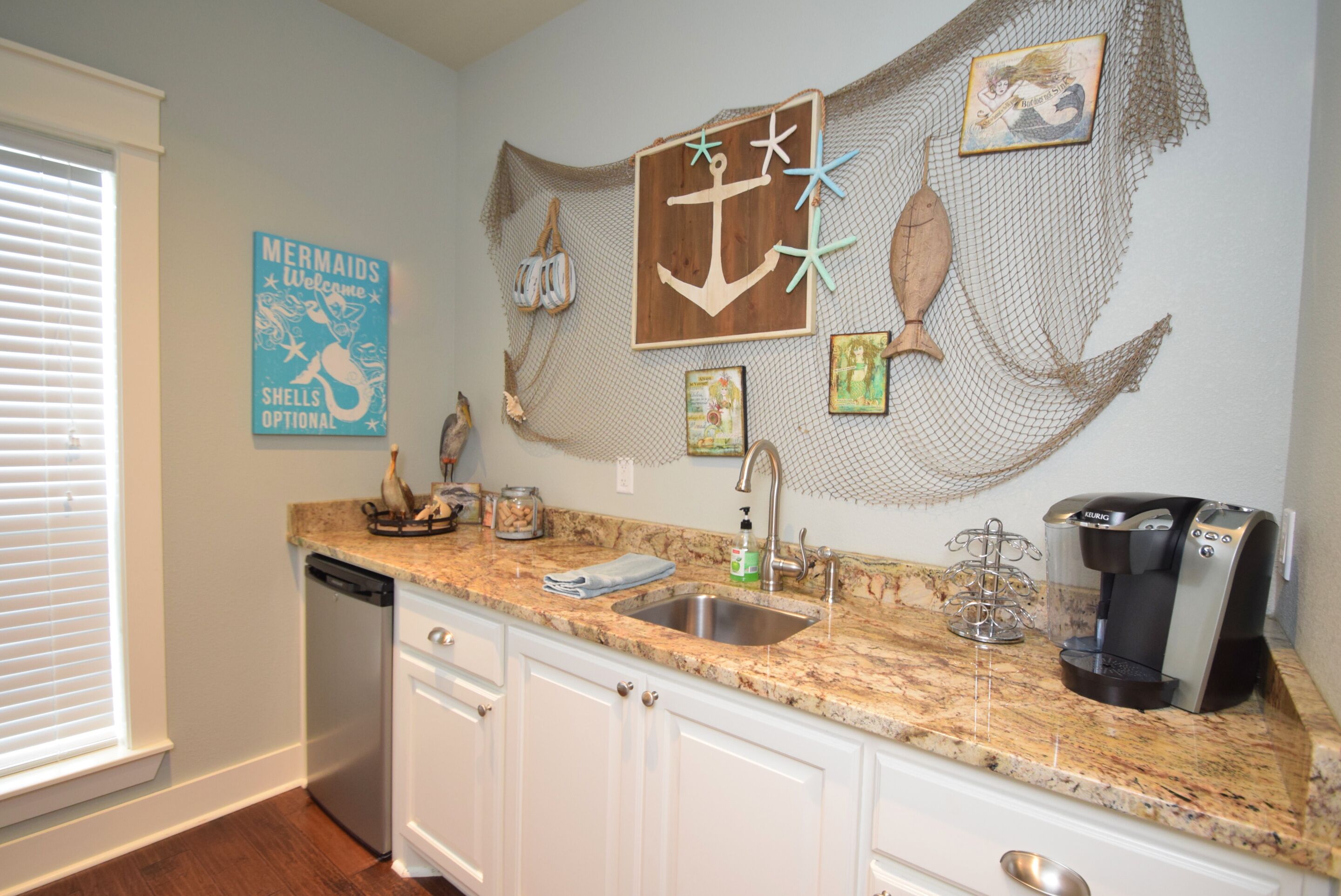 A kitchen with white cabinets, a granite countertop, a coffee maker, and a decorative wall with nautical-themed artwork.