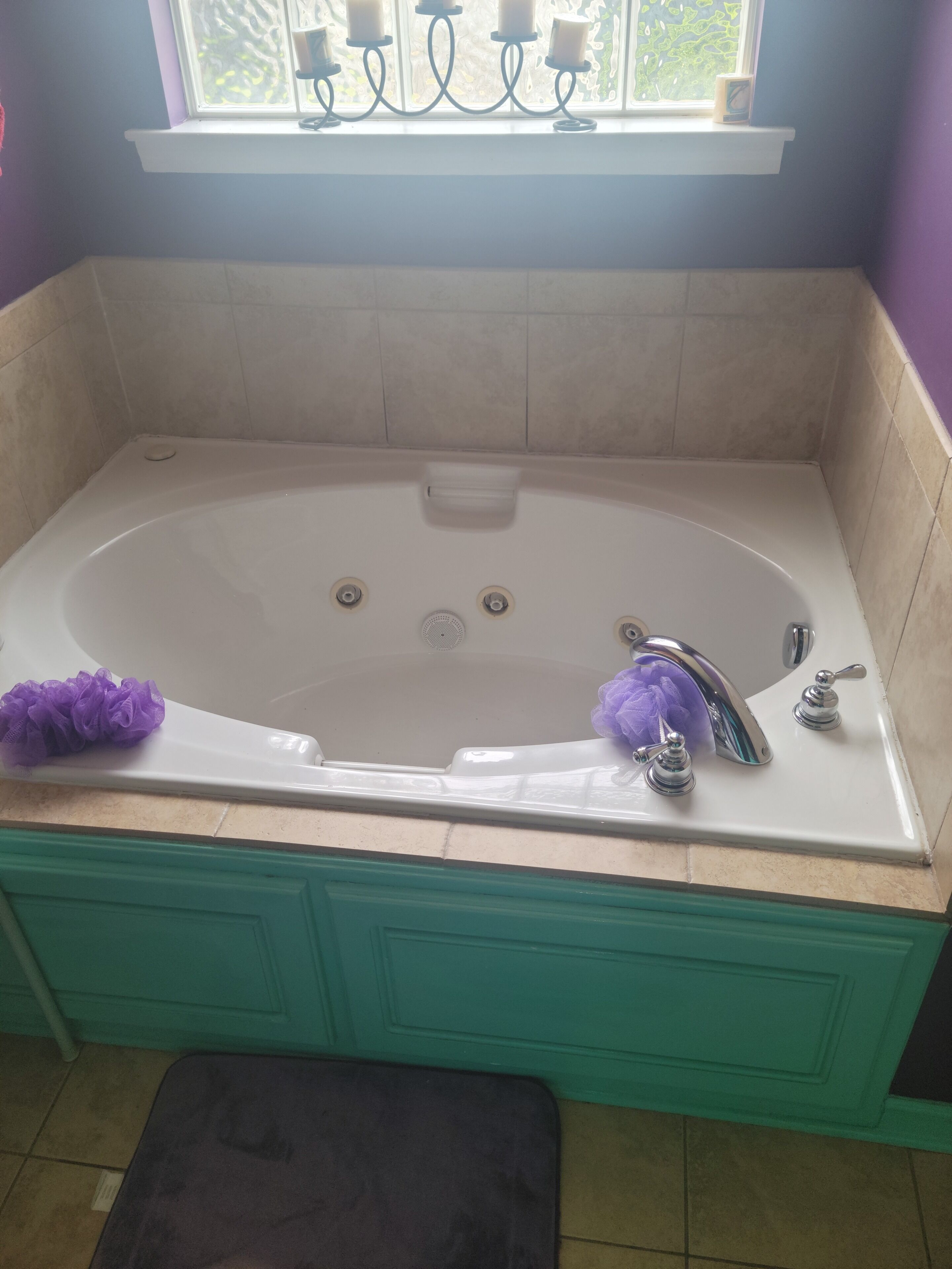 A bathroom with a large bathtub, a window with a view, and a shelf with candles.