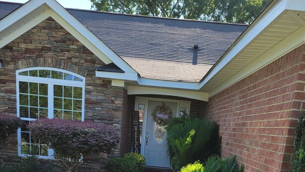 A house with a stone facade, a front door with a 'Welcome' sign, a small front yard with grass and shrubs, and a concrete driveway leading to the entrance. - HOME AWAY FROM HOME FOR THE MASTERS (Augusta)