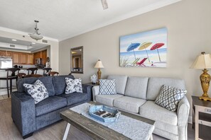 A living room with a grey sofa, a coffee table, and a painting of beach umbrellas. - Seawind 1308 by Liquid Life (Gulf Shores)