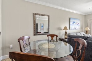 A dining area with a glass table and wooden chairs, a sofa, and a painting on the wall. - Seawind 1308 by Liquid Life (Gulf Shores)