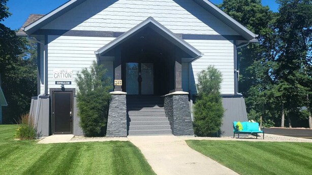 A white building with a gabled roof, a front entrance with steps, and a small porch area.