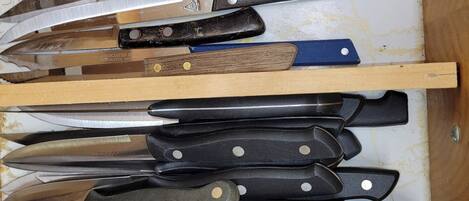 A drawer containing various knives with wooden handles and metal blades, organized on shelves.