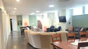 A spacious living area with a large sectional sofa, a dining table with chairs, and a flat-screen TV mounted on the wall.