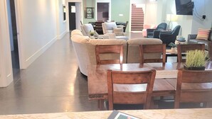 A spacious living room with a large wooden table, multiple seating options, and a view of a staircase leading to another level.