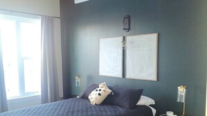 A bedroom with a large bed, two bedside tables, a window with curtains, and two wall-mounted light fixtures.