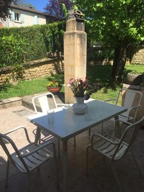 An outdoor patio with a table and chairs, a stone pillar, and a flower arrangement. - Studio in Sarlat, for a couple in search of calm (Sarlat-La-Canéda)