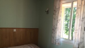 A single bed in a room with a wooden headboard, a window with floral curtains, and a green wall. - Studio in Sarlat, for a couple in search of calm (Sarlat-La-Canéda)