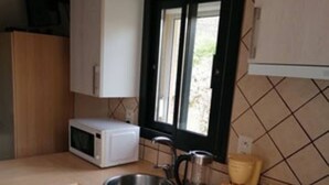 A compact kitchen with white cabinets, a microwave, a gas stove, a sink, and a window with a view of greenery outside. - Studio in Sarlat, for a couple in search of calm (Sarlat-La-Canéda)
