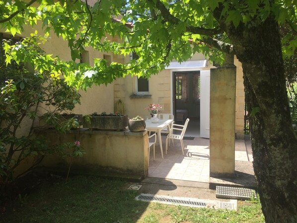 A patio area with a table and chairs, surrounded by greenery and a building with a yellow wall. - Studio in Sarlat, for a couple in search of calm (Sarlat-La-Canéda)