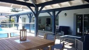Ein überdachter Außenbereich mit Pool, Holztisch und Stühlen.
