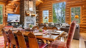 L’intérieur d’une cabane en rondins, avec une cheminée en pierre, une table à manger en bois et un coin salon confortable, comprenant un canapé et un téléviseur.