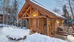 Une cabane en rondins avec un toit enneigé, une façade en bois et une véranda avec des sièges.