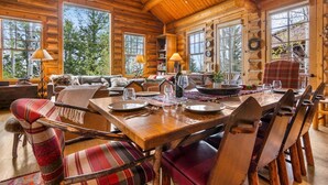 L’intérieur d’une cabane en rondins, avec un coin repas, des meubles en bois et de grandes fenêtres.