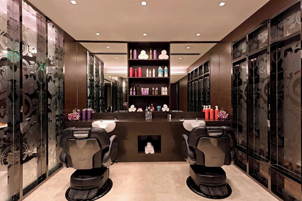 A modern salon with two black salon chairs, a central counter with various hair products, and decorative mirrors on the walls.