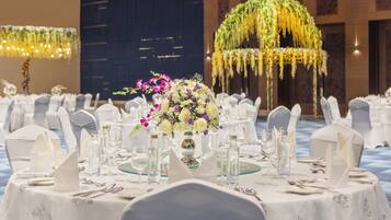 Un salón de banquetes con mesas redondas dispuestas para un evento formal, con manteles blancos, cristalería y centros de mesa florales.