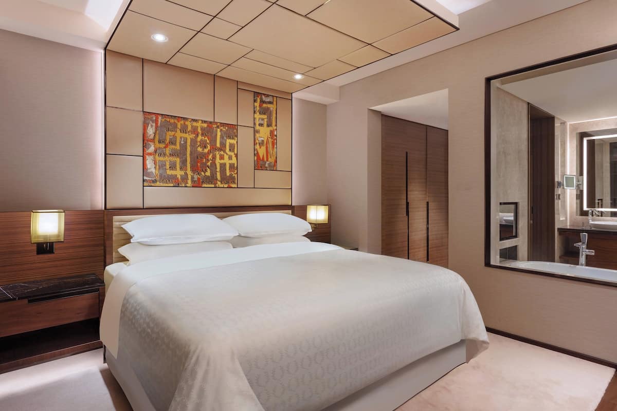 Habitación de hotel con una cama grande, una mesita de noche, una obra de arte colgada en la pared, un armario y un espejo amplio.