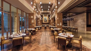 Un vaste espace de restauration d’hôtel, doté de nombreuses tables et chaises, de grandes fenêtres et d’un aménagement intérieur moderne.