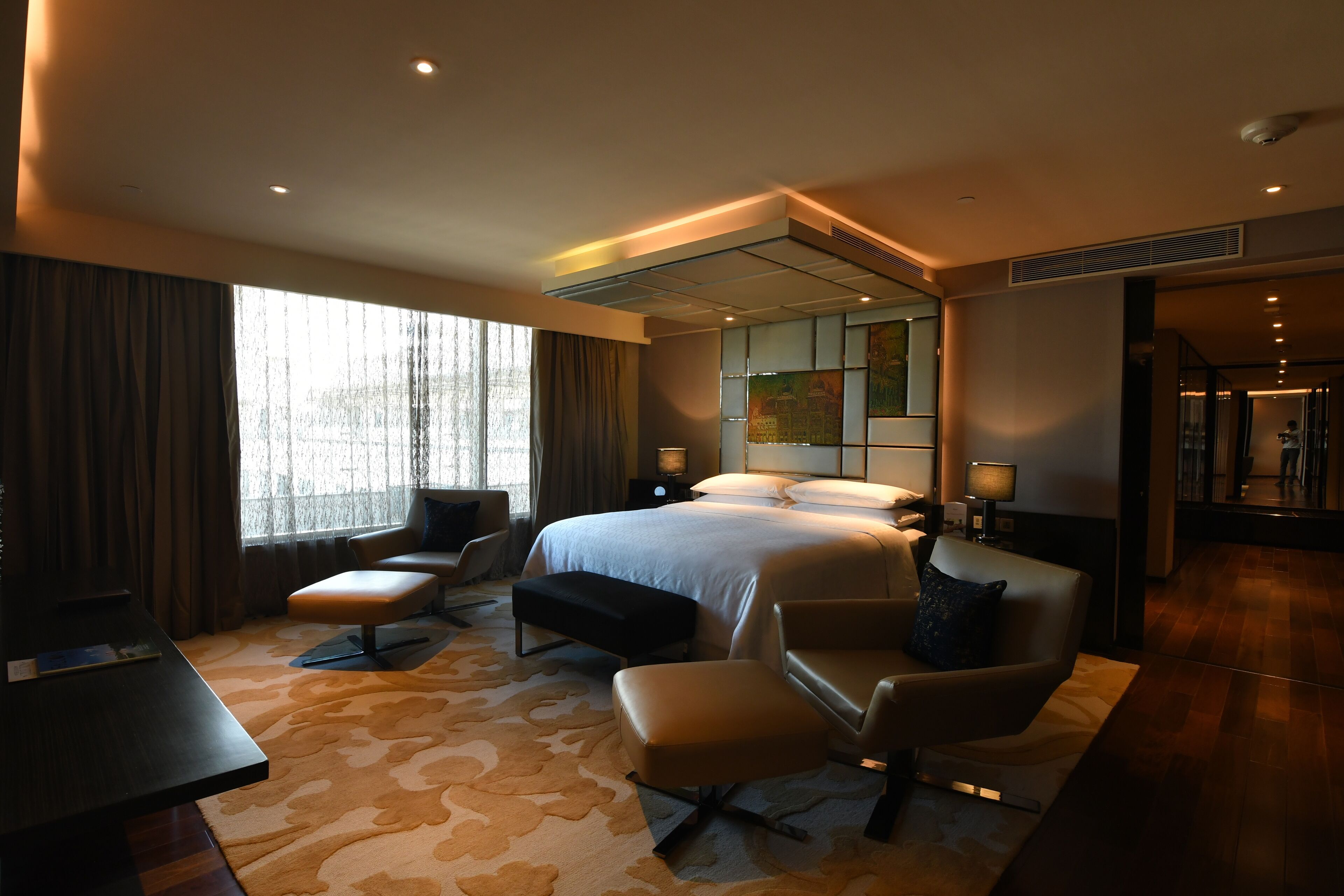 A modern hotel room with a large bed, a desk, a chair, and a sofa.