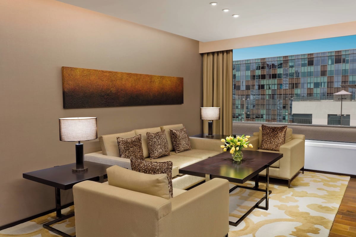 Una habitación de hotel moderna con un conjunto de sofá, una mesa de centro, una lámpara y un ventanal con vistas a un edificio.