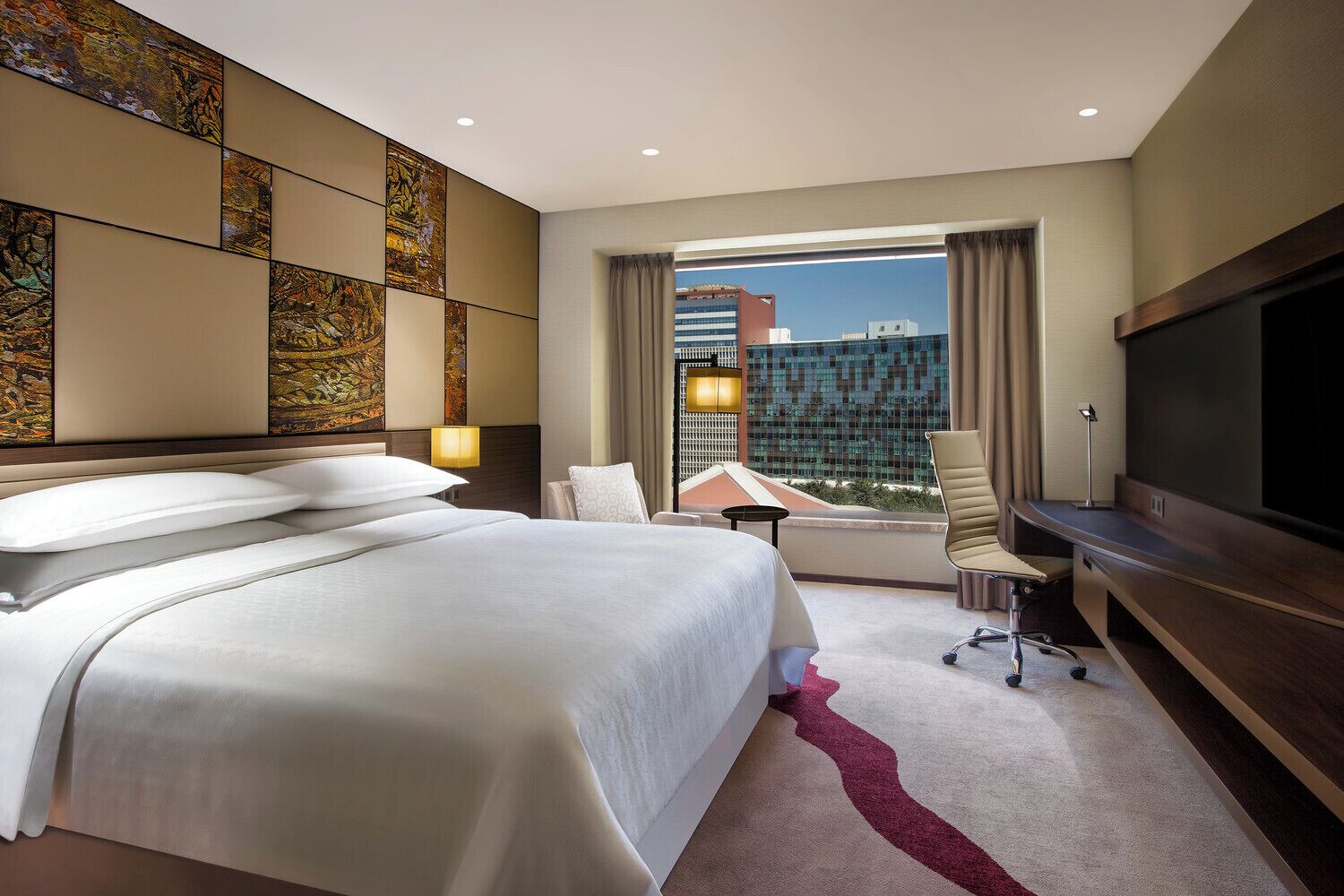 A hotel room with a large bed, a desk, a TV, and a view of the cityscape.