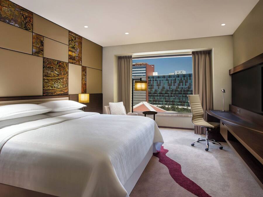 A hotel room with a large bed, a desk, a TV, and a view of the cityscape.