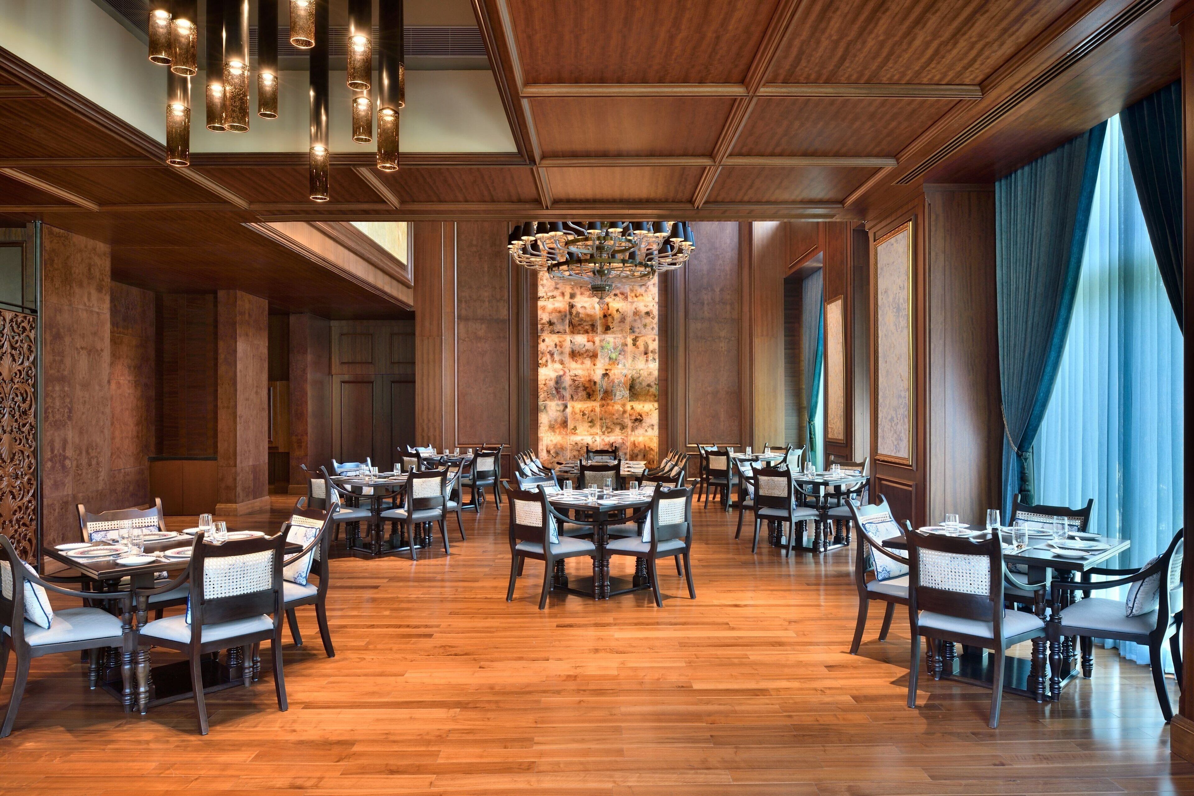 A spacious dining area with multiple tables and chairs, a central chandelier, and wooden paneling on the walls and ceiling.