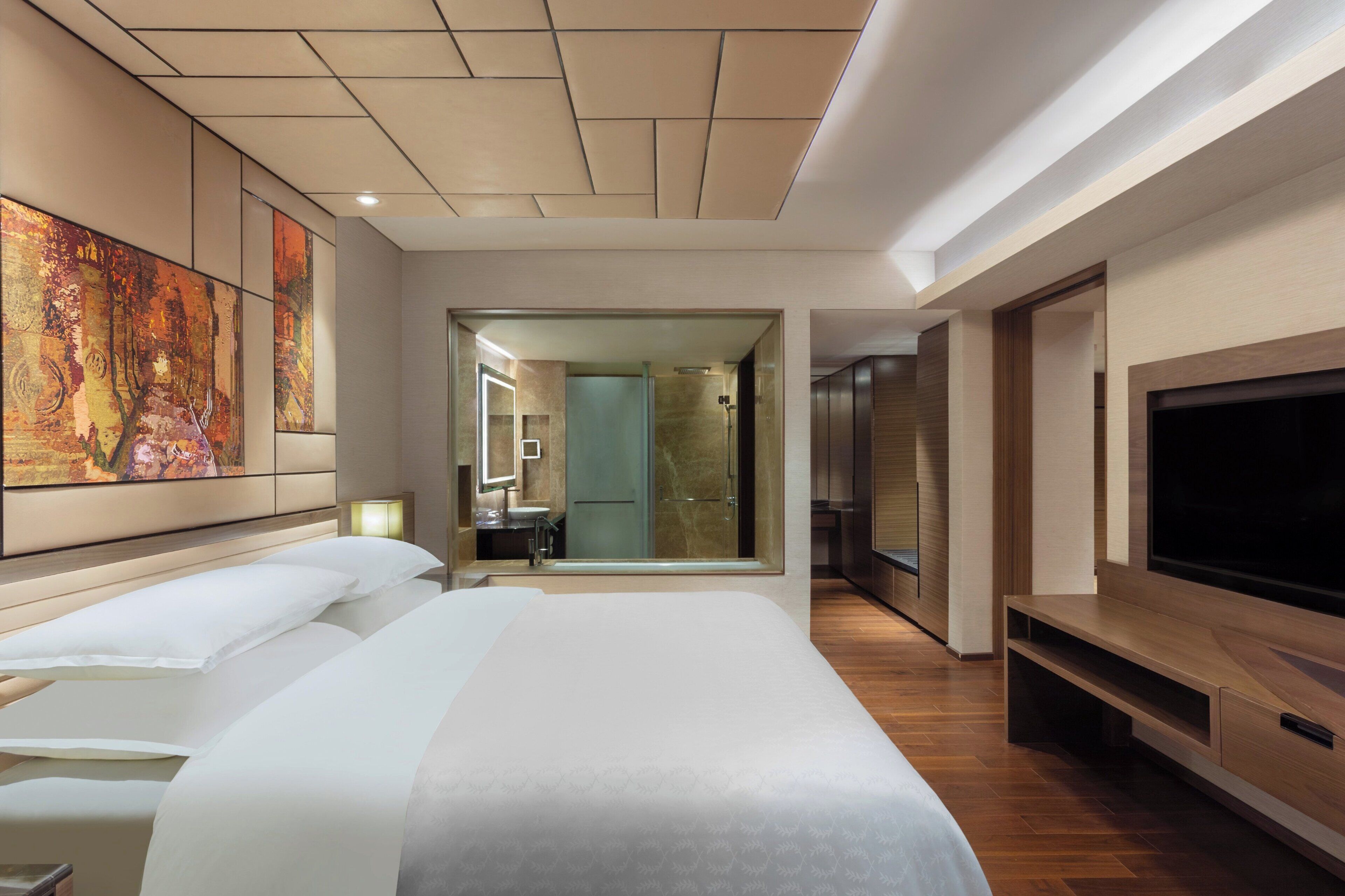 Habitación de hotel con una cama grande, televisión y baño visible a través de una puerta abierta.