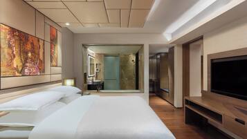 Habitación de hotel con una cama grande, televisión y baño visible a través de una puerta abierta.