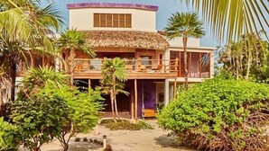 Un bâtiment à deux étages, doté d’un toit de chaume, entouré d’une végétation luxuriante et de palmiers.