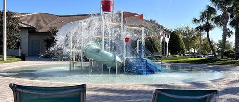 Un parque acuático con un tobogán de agua, un cubo rojo y dos sillas verdes.